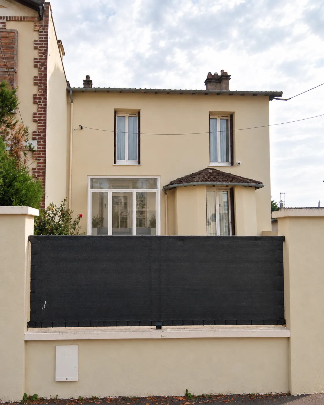 Vue de la rue : l’entrée fermée sous l’auvent, derrière le mur de clôture.
